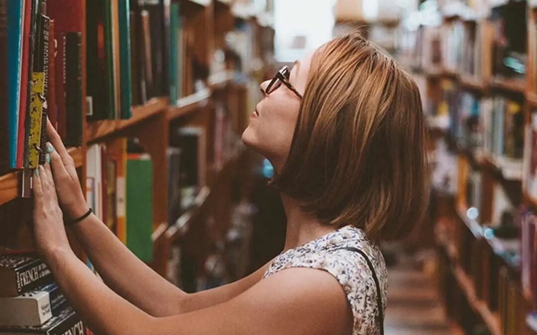 Adult with glasses browsing a shelf of books