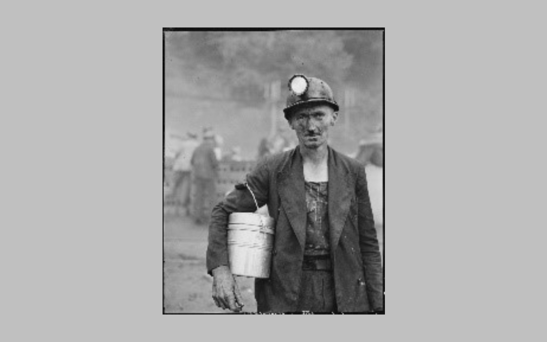 Old BW photo of a coal miner with a light on his head and a lunch bucket