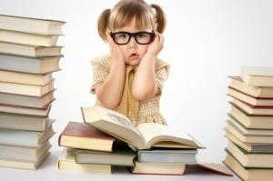 Photo of a young girl with oversized black glasses, looking dismayed with stacks of books around her