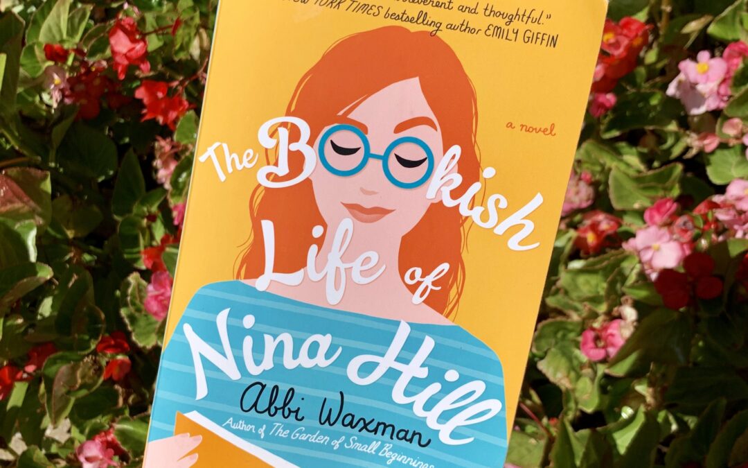 Photo of an individual holding the book "The Bookish Life of Nina Hill" by Abbi Waxman. Red flower background.