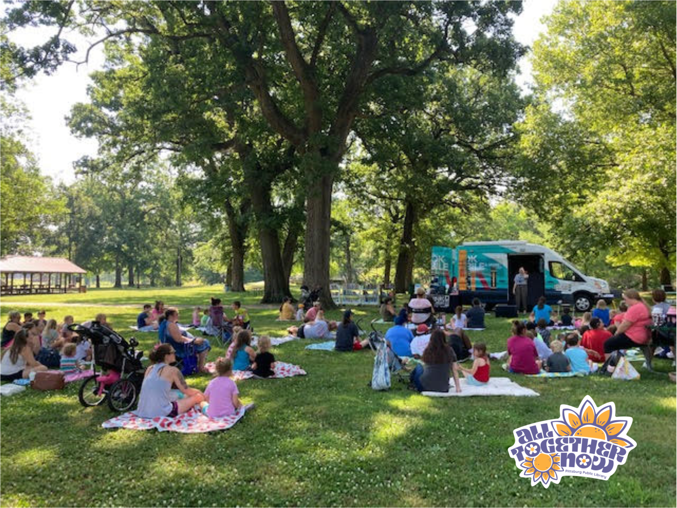 Photo of an outdoor photo of Story Time in the park, with the PPL Bookmobile. The "All Together Now" logo is in the bottom right corner.