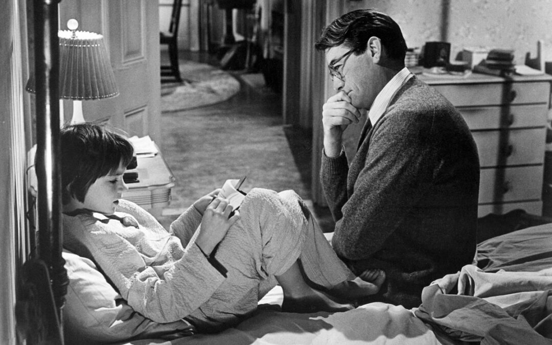 Movie still from "To Kill a Mockingbird" (1962). In this scene, Scout Finch (Mary Badham), age 6, is sitting up in her bed with a book propped on her lap. Her father, Atticus Finch, (Gregory Peck), sits at foot of her bed, intently listening to Scout.