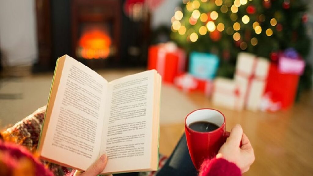 Stylized photo of a person reading a book with a cup of coffee/tea in front of a holiday tree